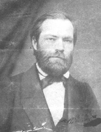 Kuva 3. Carl Oscar Malm (1826–1863). – Kuurojen Liitto ry, Kuurojen museo. Mustavalkoinen rintakuva parrakkaasta tummahiuksisesta miehestä jolla puku - valkoinen paita ja musta puvuntakki - rusetti kaulassa.